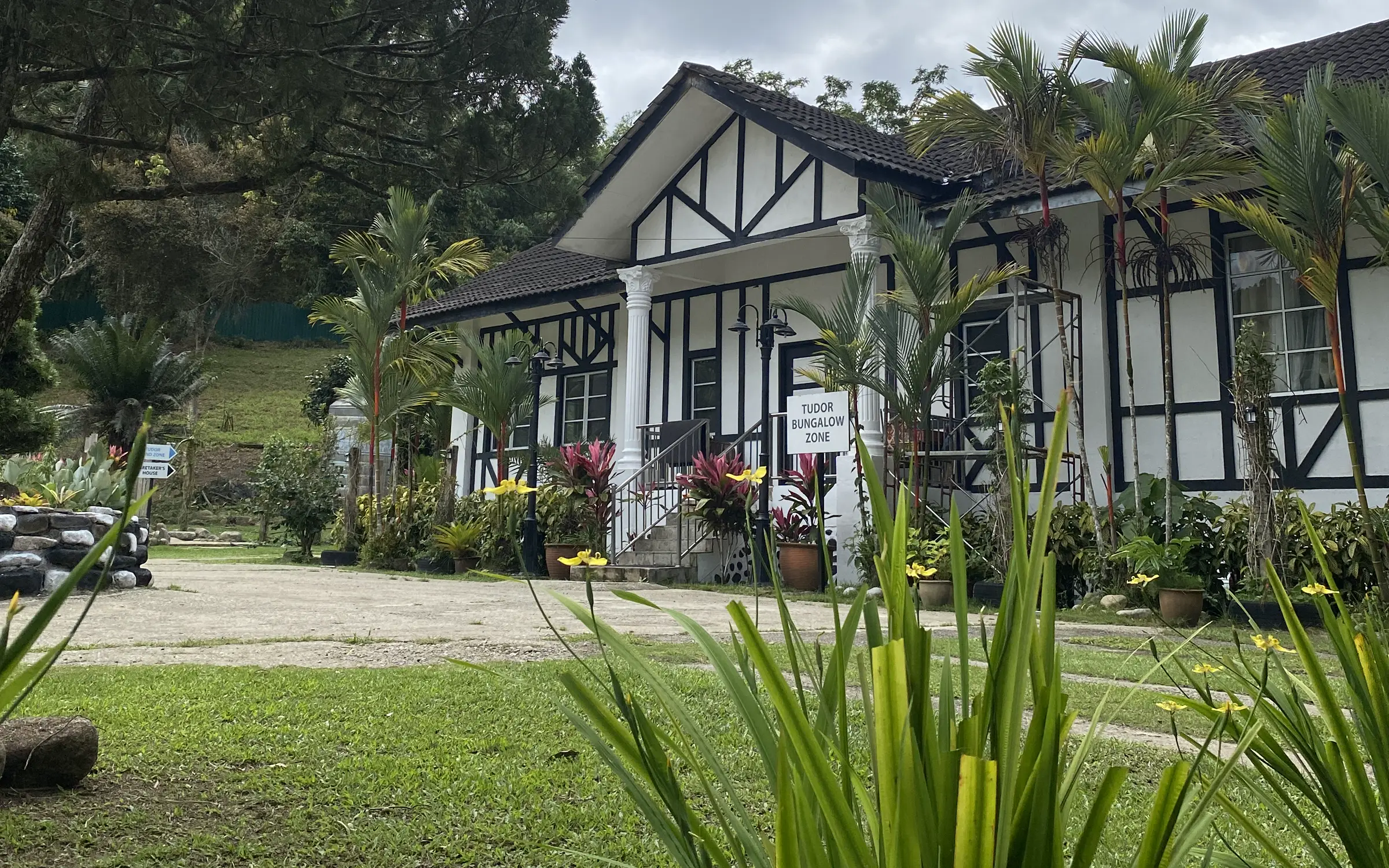 Le' Manah's black-and-white Tudor bungalow seen through garden leaves, with forested hills behind